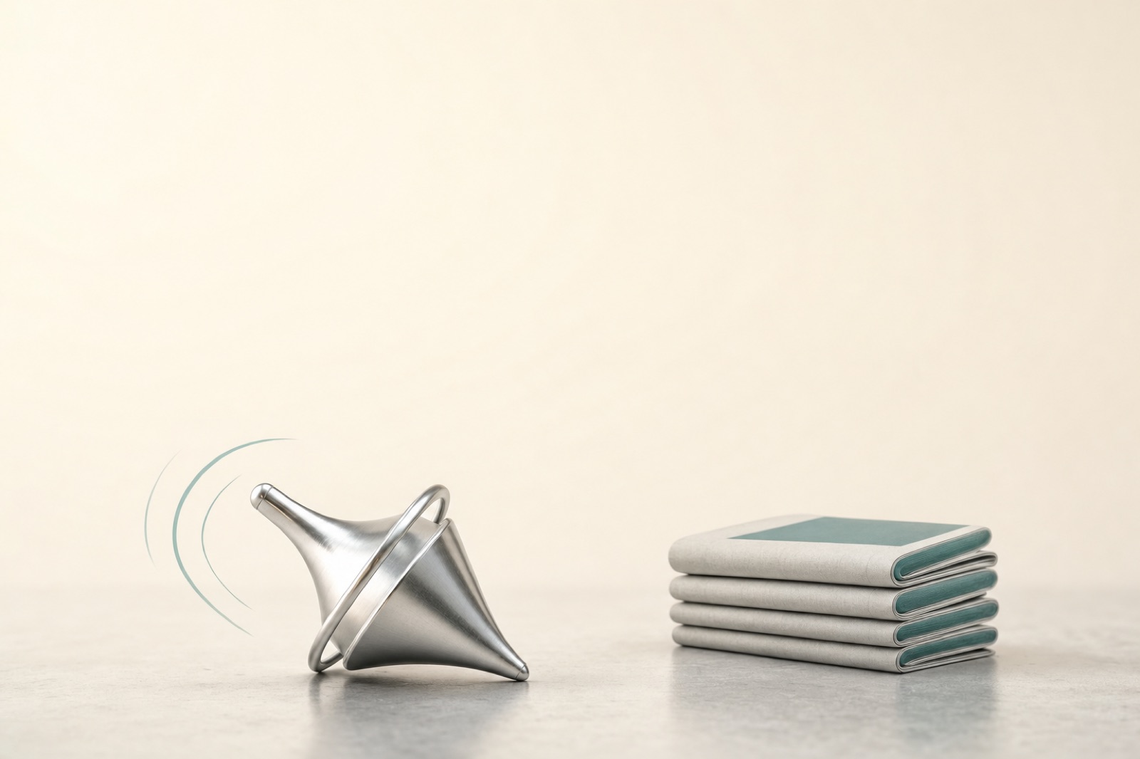 A silver spinning top lying on its side beside a neat stack of folded pages.